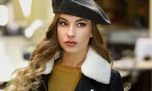 Elegancka kobieta w grafitowym beretu, z burzą blond loków i w czarnej ramonesce. Dowiedz się, jak nosić beret damski, by wyglądać stylowo.