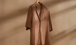 Brązowa, lniana koszula na drewnianym wieszaku. Idealna baza do letnich stylizacji, dodaje lekkości i elegancji.