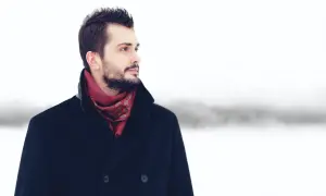 Mężczyzna w granatowym płaszczu i czerwonym, wzorzystym szaliku, na tle zimowego krajobrazu. Idealny przykład, jaki szalik do granatowego płaszcza.