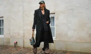 Elegancka stylizacja z czapką z daszkiem. Kobieta w czarnym garniturze i płaszczu, z torebką i modną czapką.