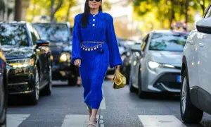 Elegancka kobieta w chabrowej sukience i fioletowych sandałkach na obcasie, z złotą torebką. Idealne buty do chabrowej sukienki to te, które podkreślą jej urok.