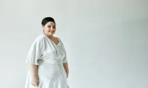 Piękna kobieta w białej sukni z dekoltem V i zdobionym pasem. Idealny fason sukienki dla puszystej, podkreślający sylwetkę.