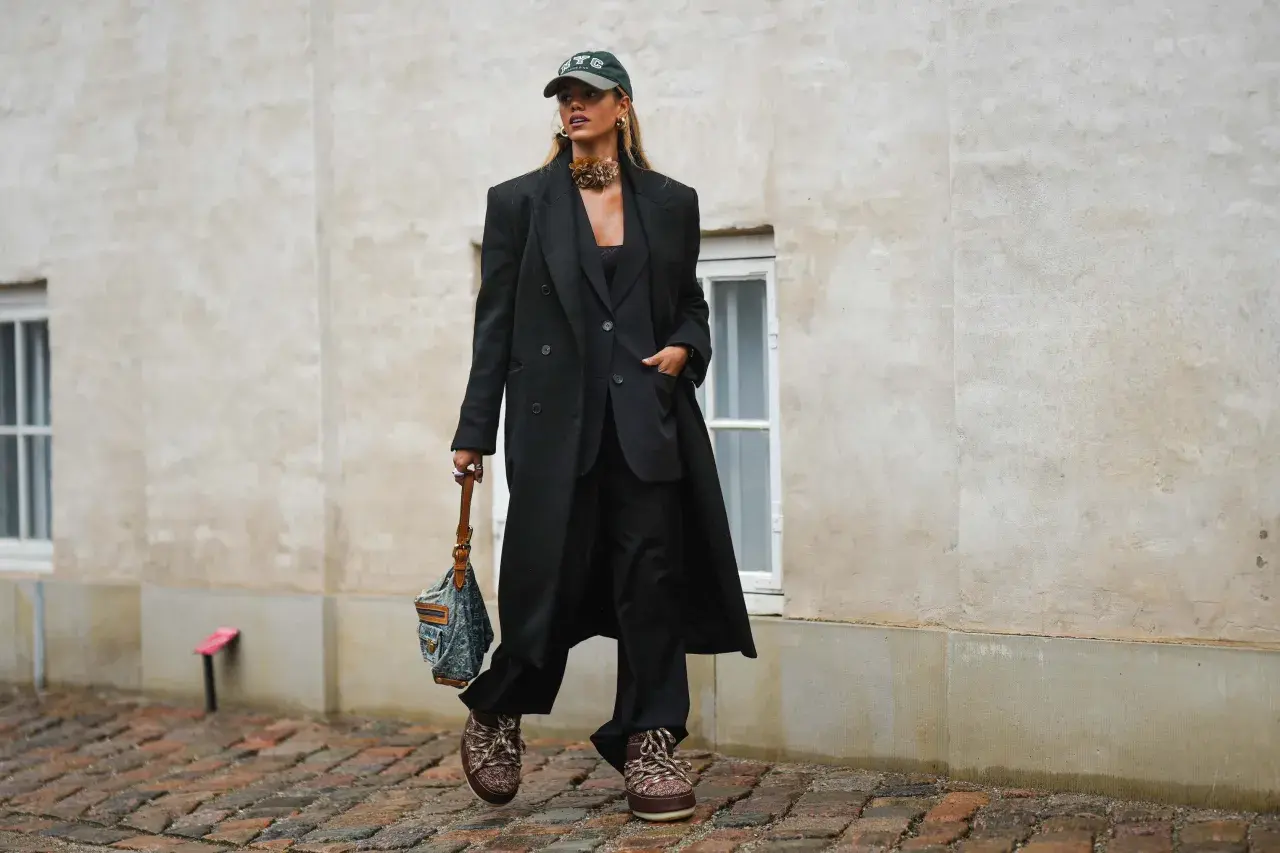 Elegancka stylizacja z czapką z daszkiem. Kobieta w czarnym garniturze i płaszczu, z torebką i modną czapką.