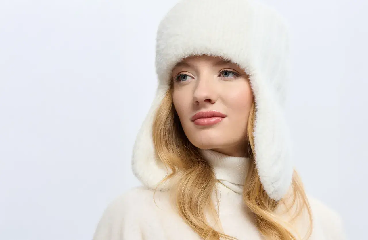 Blondynka w białej, futrzanej czapce uszatce, prezentującej najmodniejsze nakrycia głowy.