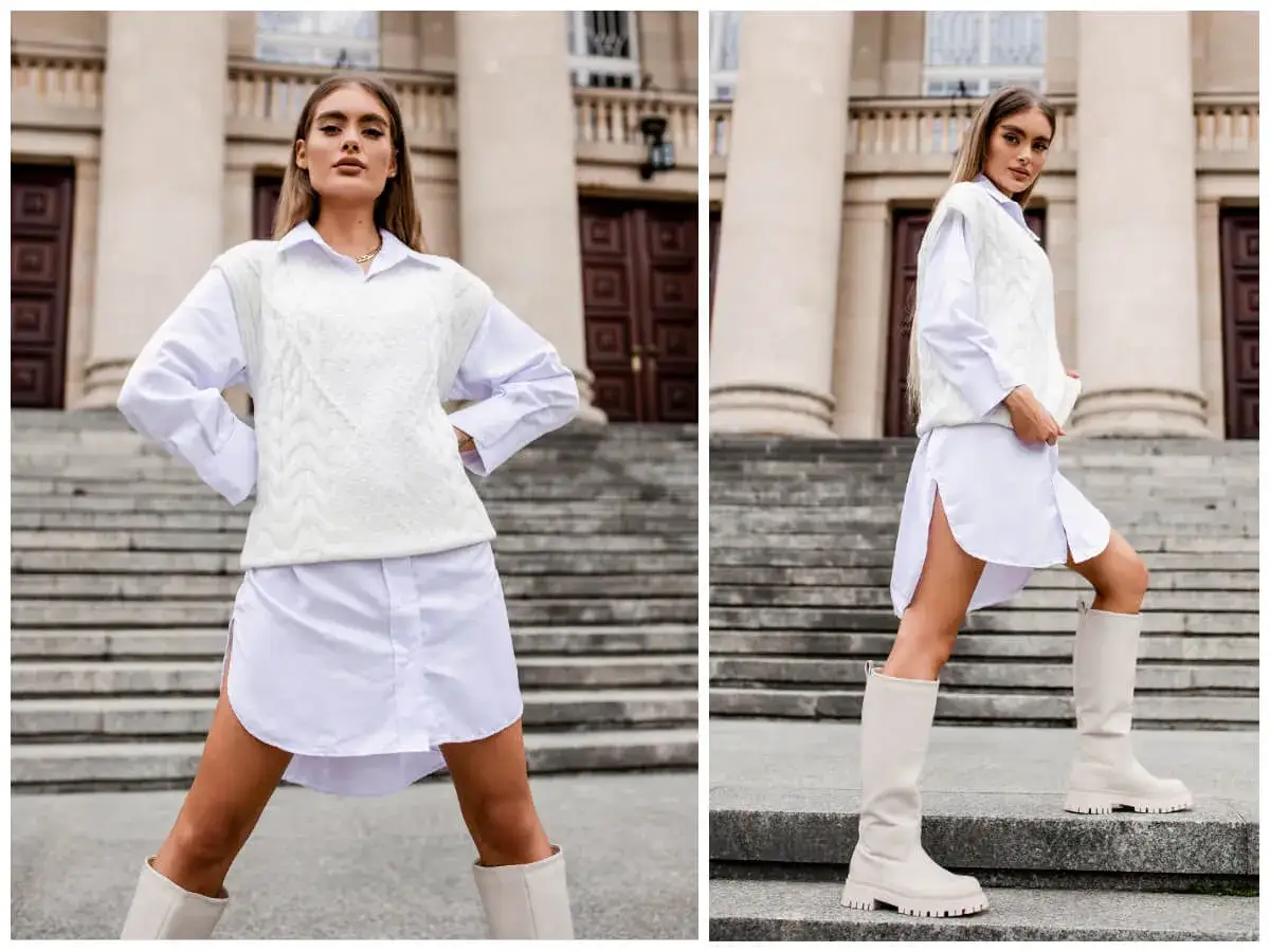 Elegancka biała kamizelka stylizacje z koszulą i kozakami. Modelka prezentuje modny zestaw na schodach przed budynkiem.