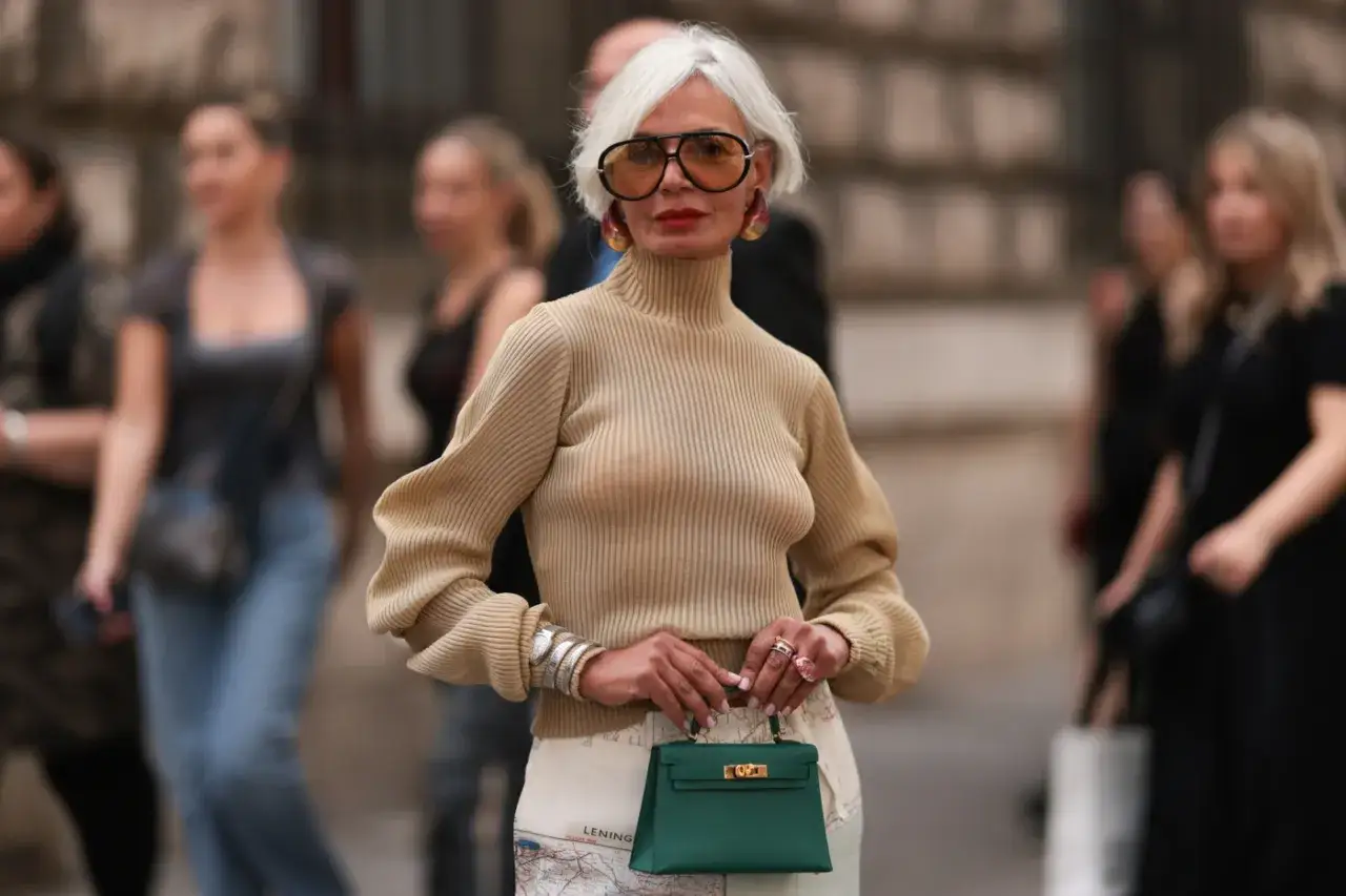 Elegancka kobieta 60 plus w beżowym golfie i spódnicy z mapą, trzymająca zieloną torebkę. Stylowa moda 60 plus.