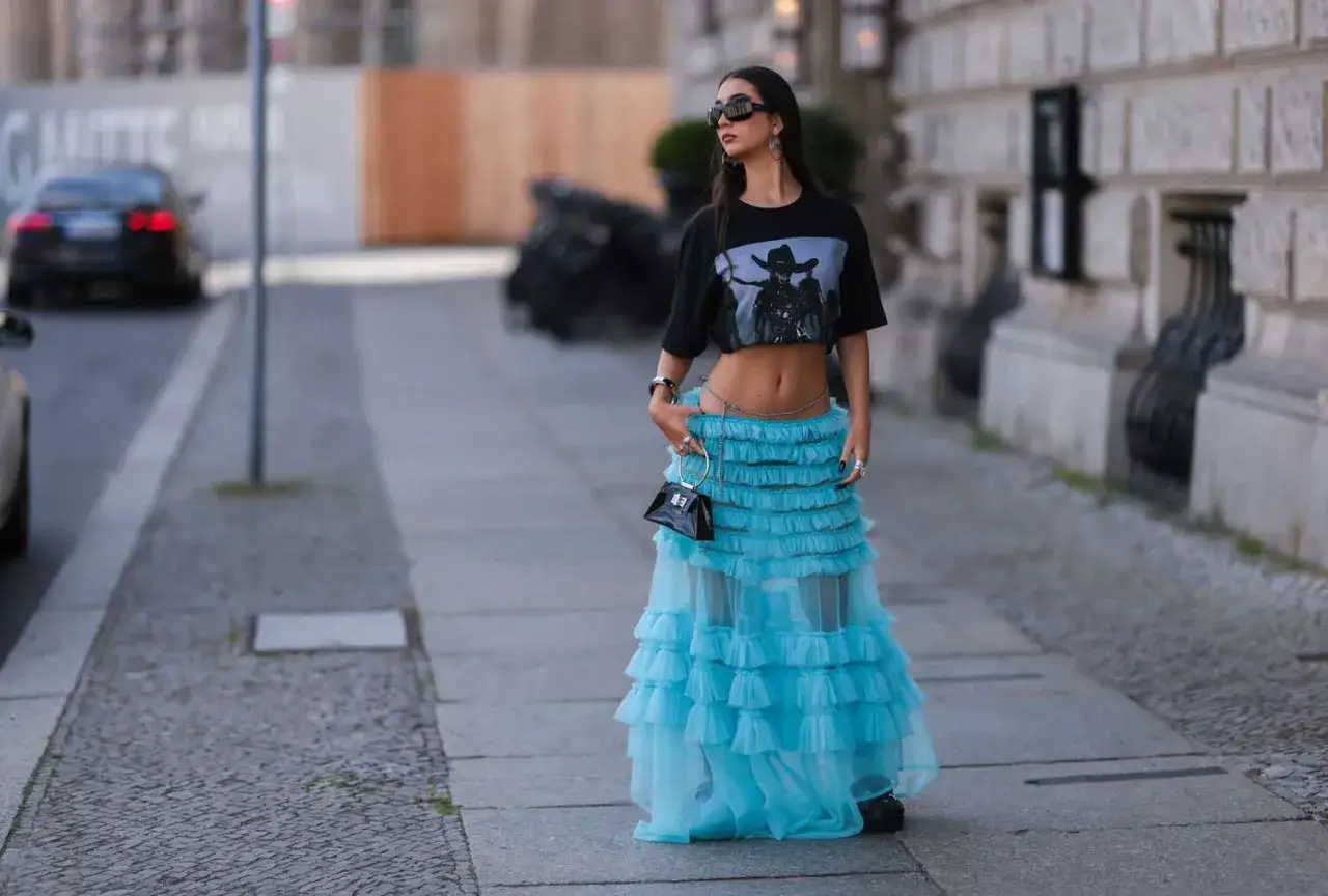 Kobieta w turkusowej, falbaniastej spódnicy tiulowej i krótkim T-shircie prezentuje odważne stylizacje.