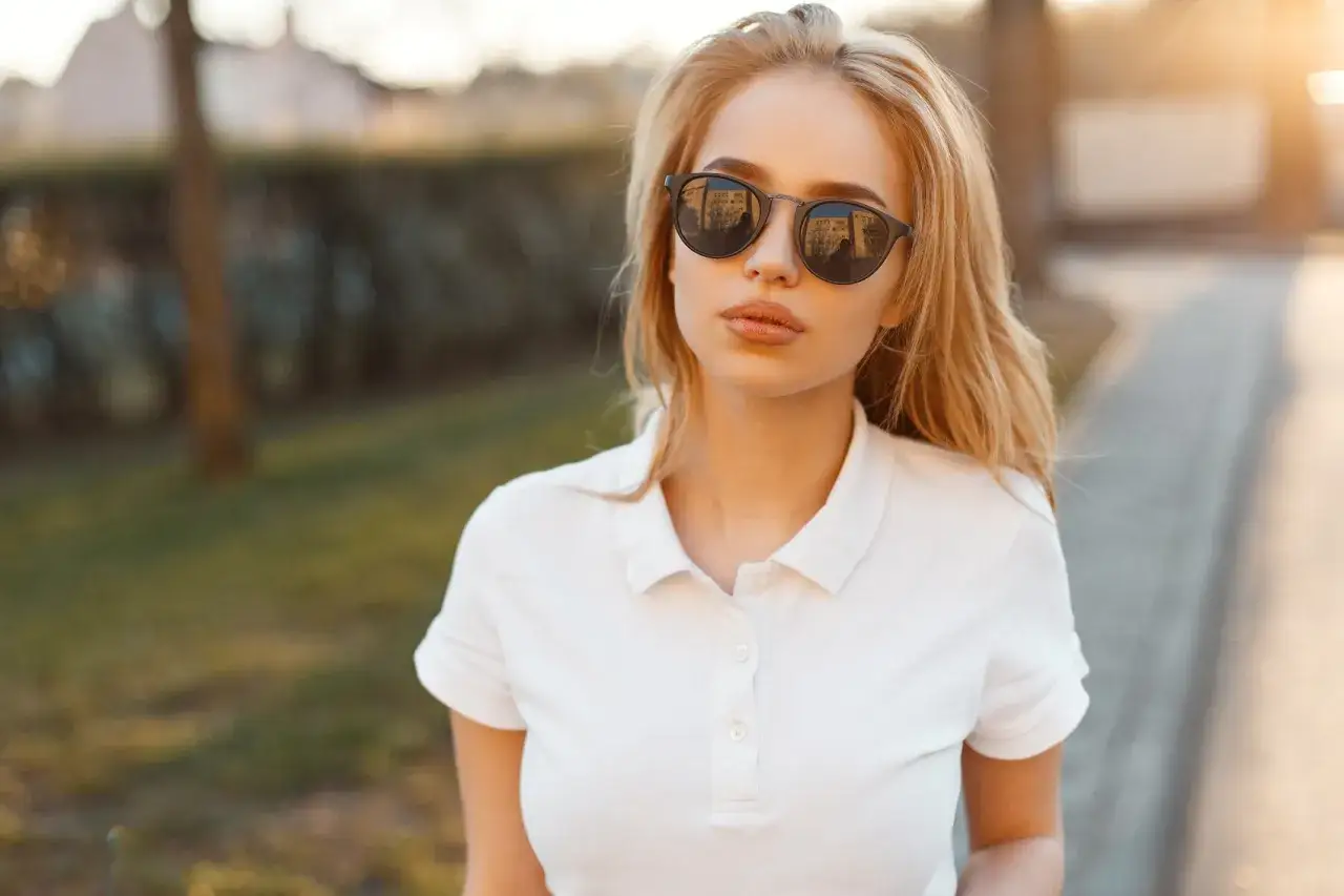 Blondynka w okularach przeciwsłonecznych i białej koszulce polo. Stylowa inspiracja, jak nosić koszulka polo damska na co dzień.