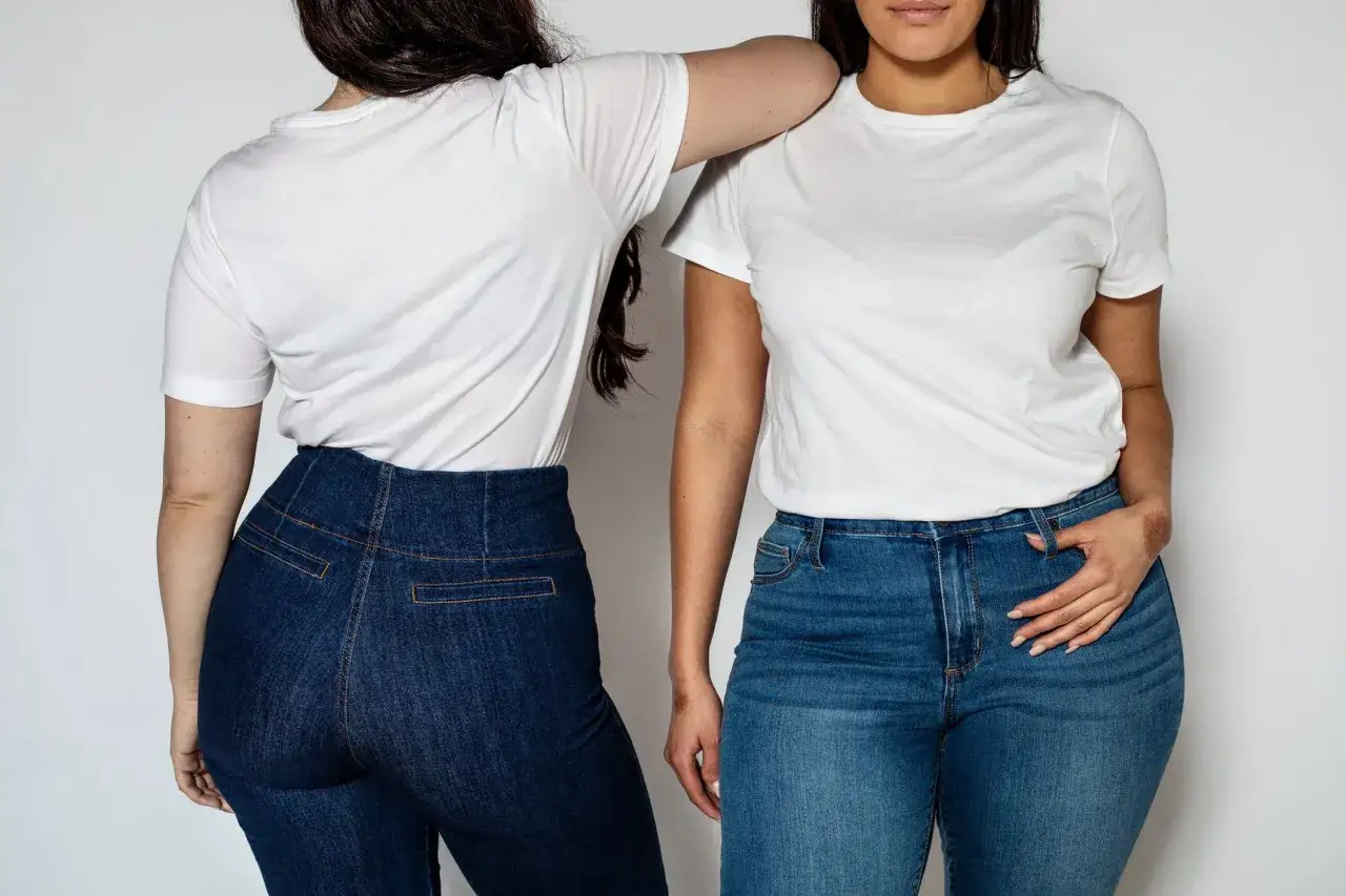 Dwie kobiety w białych T-shirtach i jeansach. Jedna ma ciemne jeansy z wysokim stanem, idealne jako spodnie dla grubych ud.