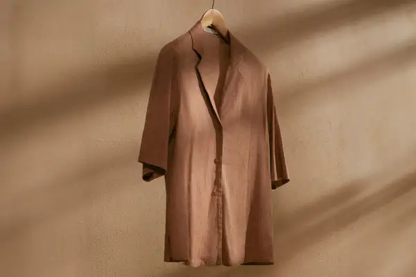 Brązowa, lniana koszula na drewnianym wieszaku. Idealna baza do letnich stylizacji, dodaje lekkości i elegancji.