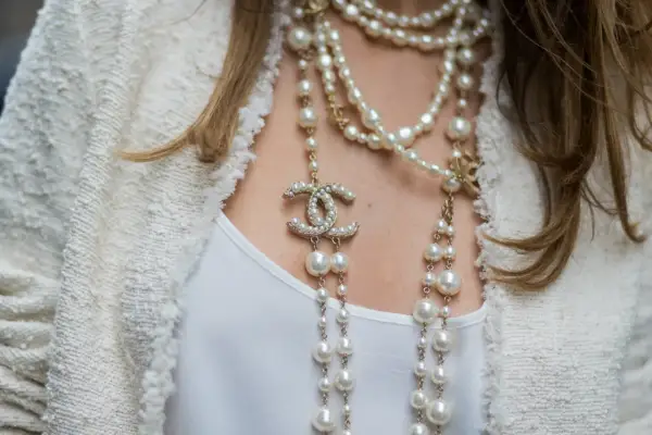 Eleganckie stylizacje z perłami: wielowarstwowy naszyjnik z logo Chanel i perłami na tle białej marynarki.